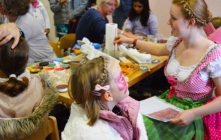 Eine Mitarbeiterin im Dirndl beim Kinderschminken auf einem Oktoberfest im Kinder- und Jugendwohnhaus Allerheiligen der Lebenshilfe Neuss.