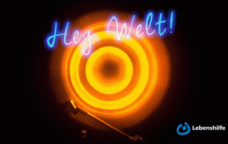 Ansicht eines Plattenspielers von oben vor einem schwarzen Hintergrund. Darüber steht in leuchtenden blauen Buchstaben "Hey Welt".