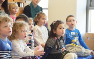 Eine Gruppe Kita Kinder der Lebenshilfe Neuss sitzt in einer Kita und lauscht dem Konzert.
