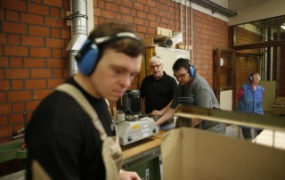Junge Menschen mit einer Behinderung arbeiten mit Ohrschutz in einer Werkstatt.