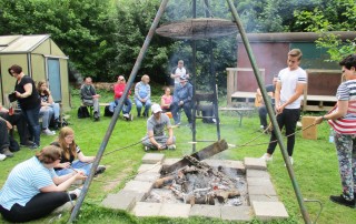 Nutzer und Mitarbeiter der Lebenshilfe Neuss machen Stockbrot im Freien an einer großen Feuerstelle.