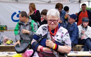 Eine Nutzerin der Lebenshilfe Neuss vor einem Stand der Lebenshilfe Neuss. Im Hintergrund sind weitere Nutzer zu sehen.