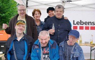 Gruppenbild von Nutzern und Mitarbeitenden der Lebenshilfe Neuss vor einem Stand der Lebenshilfe Neuss.