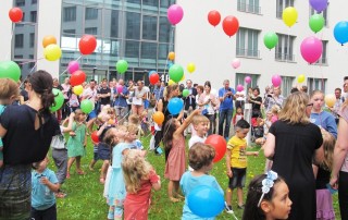 Viele Kinder, Besucher und Mitarbeiter der Lebenshilfe Neuss bei einem Sommerfest der Kita Hammfeld, die bunte Luftballons steigen lassen.