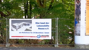 Baustellenplakat mit der Aufschrift: " Hier baut der Lebenshilfe Neuss E.V. ein Wohnhaus für 24 Bewohner/-innen.