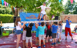 Kinder führen eine Zirkus-Nummer auf, auf dem Sommerfest im Familienzentrum Am Baldhof. Ein Kind balanciert auf einer Leiter.