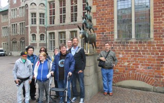 Gruppenbild der Nutzer des UWos der Lebenshilfe Neuss bei einem Städtetrip nach Bremen vor dem Denkmal der Bremer Stadtmusikanten.