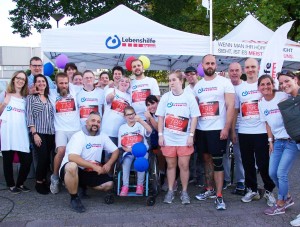 Gruppenfoto von Nutzern und Mitarbeitern der Lebenshilfe Neuss bei einem Firmenlauf. Alle tragen weiße T-Shirts mit dem Logo der Lebenshilfe Neuss.