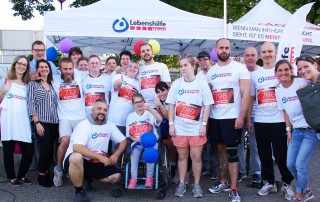 Gruppenfoto von Nutzern und Mitarbeitern der Lebenshilfe Neuss bei einem Firmenlauf. Alle tragen weiße T-Shirts mit dem Logo der Lebenshilfe Neuss.