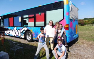 Vier Kinder stehen vor dem neu gestalteten Jugendbus.
