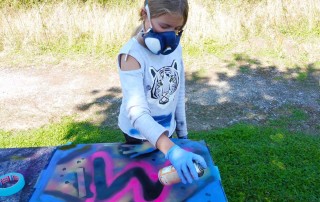 Ein Mädchen mit einer Atemschutz-Maske sprüht ein Graffiti.