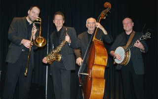 Vier Jazz-Musiker in schwarzer Kleidung auf einer Bühne vor dunklem Hintergrund.