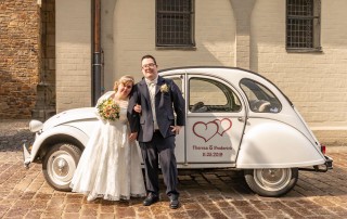 UWO-Nutzer Theresa Schulte und Frederick Breivogel in Hochzeitskleid und Anzug vor einem Oldtimer Auto.