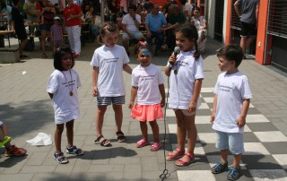Fünf Kinder treten beim Sommerfest auf. Ein Kind hält ein Mikrofon in der Hand.
