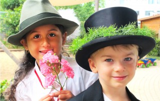 Porträt eines Mädchen und eines Jungen die beide Hüte tragen, das Mädchen hält eine Blume in der Hand. Auf dem Bild steht der Text: Wir wünschen ein sonniges, heiteres Schützenfest 2019!