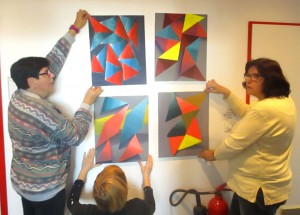 Drei Personen hängen Bilder an einer Wand auf.