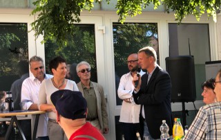 Ein Mann spricht in ein Mikrofon. Gesine Eschenburg und andere Gäste hören zu.