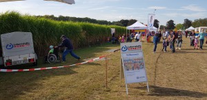 Das Familienfest im Dycker Feld. Im Hintergrund sieht man Menschen die das Fest besuchen und den Stand der Lebenshilfe Neuss. Im Vordergrund steht eine Werbetafel die auf den Stand der Lebenshilfe aufmerksam macht.