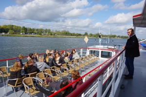 Winfried Janßen steht an der Brüstung auf einem Ausflugsschiff. Auf dem Schiff sitzen viele Mitarbeitende der Lebenshilfe Neuss.
