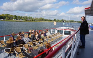 Winfried Janßen steht an der Brüstung auf einem Ausflugsschiff. Auf dem Schiff sitzen viele Mitarbeitende der Lebenshilfe Neuss.
