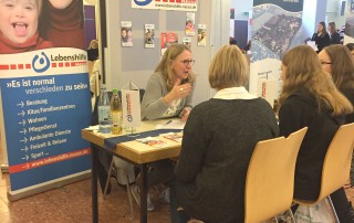 Auf der Berufsinformationsmesse im Marienhaus sitzt eine Mitarbeiterin mit zwei Besucherinnen am Stand der Lebenshilfe Neuss.
