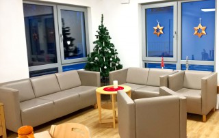 Neu gestalteter Wohnbereich mit grauen Sofas, Sesseln, einem Weihnachtsbaum und Weihnachtsdekoration.