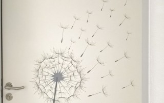 Eine Tür im neuen Wohnhaus Gnadental mit einem Wandbild darauf, auf dem eine Pusteblume zu sehen ist.