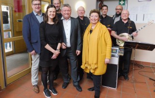 Angelika Quiring-perl, WInfried Janßen und Hermann Gröhe stehen mit Mitarbeitenden und Musikern für ein Gruppenbild zusammen.