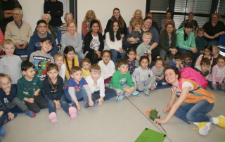 Eine große Gruppe Kinder und Mitarbeitende sieht eine Aufführung an.