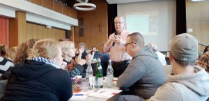 Mitarbeitende der Lebenshilfe Neuss sitzen bei einer Schulung an einem Konferenztisch und hören einem Mann zu der in ein Mikrofon spricht.