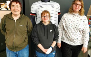 Drei Nutzerinnen bei Besuch des Fußballmuseums. Hinter ihnen steht eine Kleiderpuppe die ein Fußball-Trikot trägt.