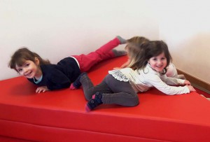 Drei Kinder toben auf roten Schaumstoff-Matten.
