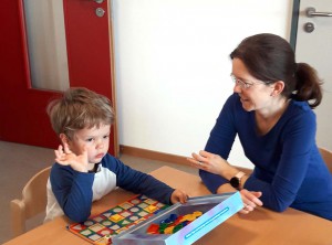 Eine Mitarbeiterin und ein Kind sitzen am Tisch und spielen.