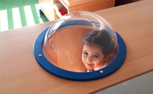 Ein Mädchen guckt durch eine Glaskuppel auf einem Klettergerüst.