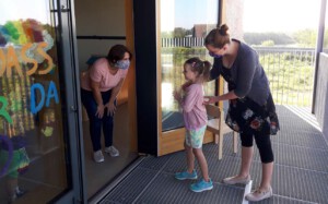 Eine Mitarbeiterin begrüßt an der Tür ein Kind, das von seiner Mutter gebracht wird.