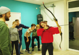 Eine Gruppe im Kinder und Jugendzentrum der Lebenshilfe Neuss sieht einem Mädchen beim Bogenschießen zu.