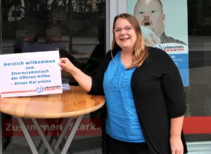 Eine Mitarbeiterin steht vor dem Lebenshilfe Center und hält ein Schild für den Elternabend hoch
