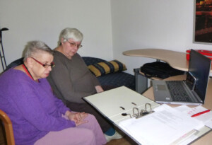 Zwei Bewohnerinnen bei einer Sitzung des Bewohner-Beirats per Videocall an einem Laptop. Vor ihnen liegen Ordner mit Dokumenten.