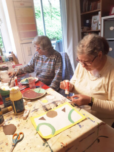 Zwei ältere Frauen sitzen nebeneinander an einem Tisch und malen.
