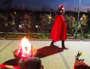 Vor der Kita Wimmelgarten steht eine Feuerschale mit einem Feuer darin. Daneben geht ein Mann, der eine St.-Martins-Verkleidung trägt.