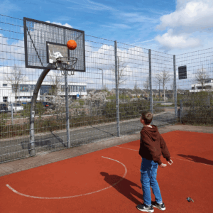 Ein Kind steht auf einem Sport-Platz und wirft einen Basket-Ball in den Korb.