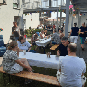 Mehrere Personen sitzen draußen an den Tischen und unterhalten sich.