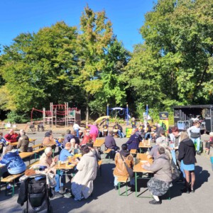 Mehrere Personen sitzen draußen auf der Bierzelt-Garnitur und hören der Band zu.