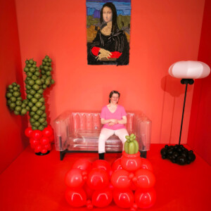 Eine Frau sitzt auf einem Kunstwerk das eine Couch ist und das steht in einem Zimmer was auch ein Kunstwerk ist.