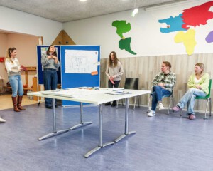 Eine Frau präsentiert mehreren Personen im Raum die Inhalte einer Präsentation.