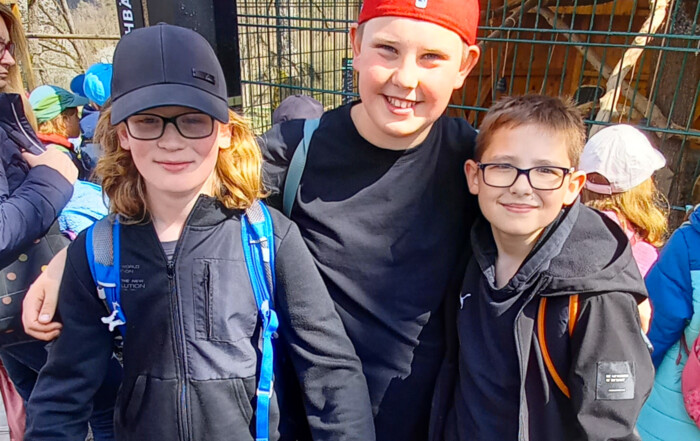 Gruppenfoto von drei Kindern die in die Kamera blicken vor Wildtier-Gehege.