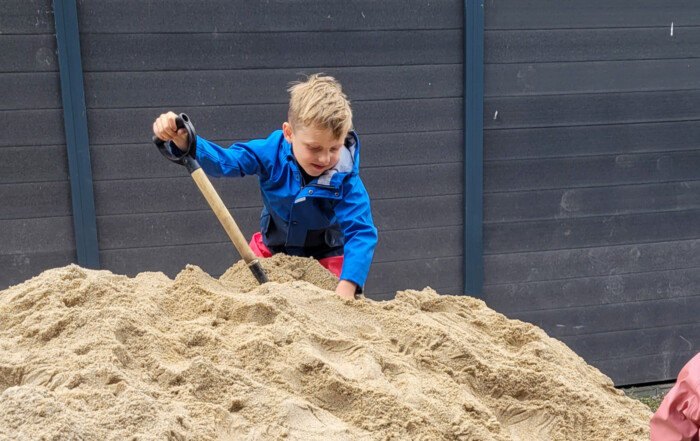 Ein Kind steht auf einem Sand-Berg und schaufelt den Sand weg.