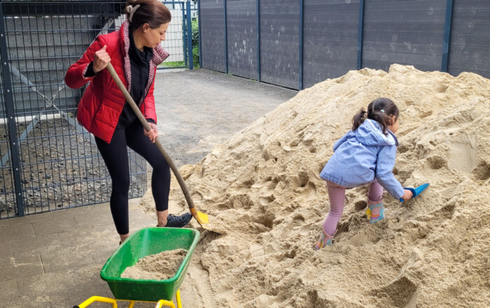 Eine Mutter und ein Kind schaufeln Sand in eine Schubkarre.