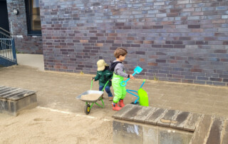 Zwei Kinder kippen den Sand in den Sandkasten rein.