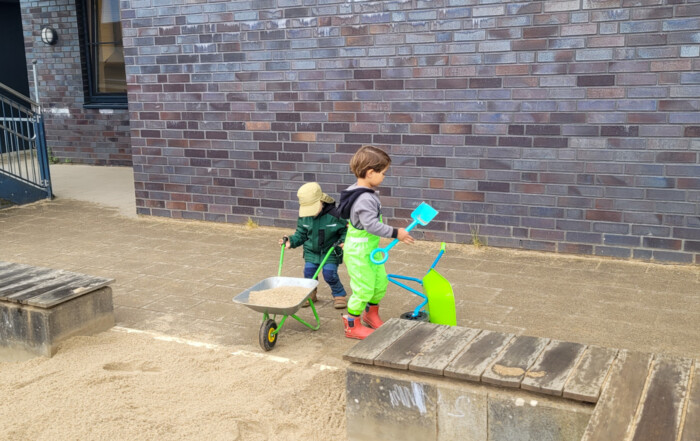 Zwei Kinder kippen den Sand in den Sandkasten rein.